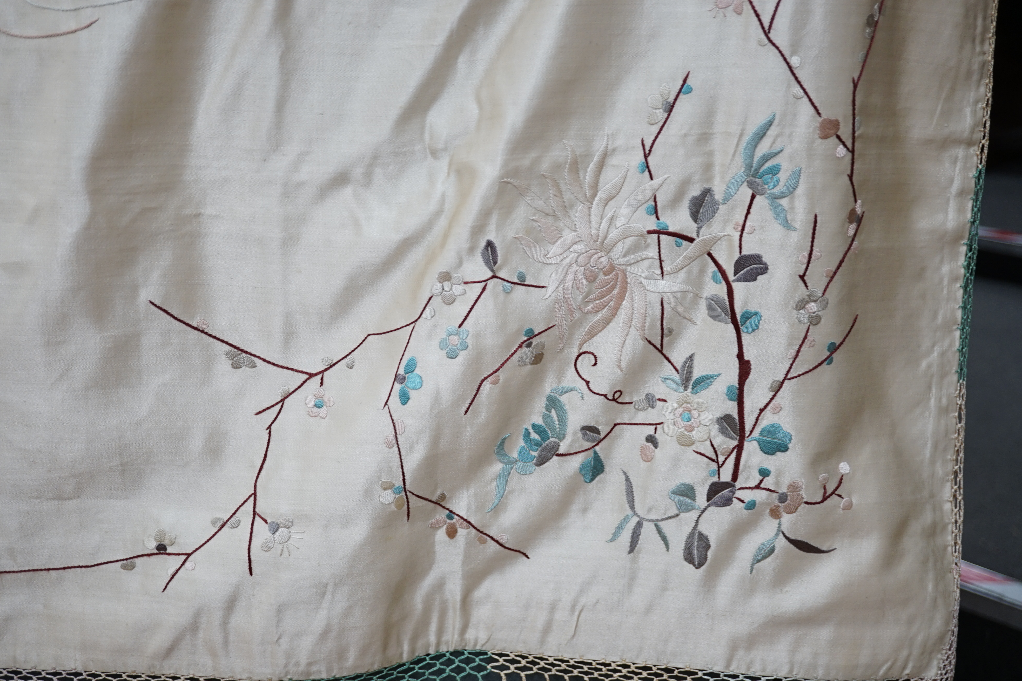 A 1920’s-30’s Chinese oyster silk satin embroidered shawl, now converted to a wall hanging, embroidered in pastel coloured silk threads, the large central motif of two dragons playing with a pearl, the corners of the han